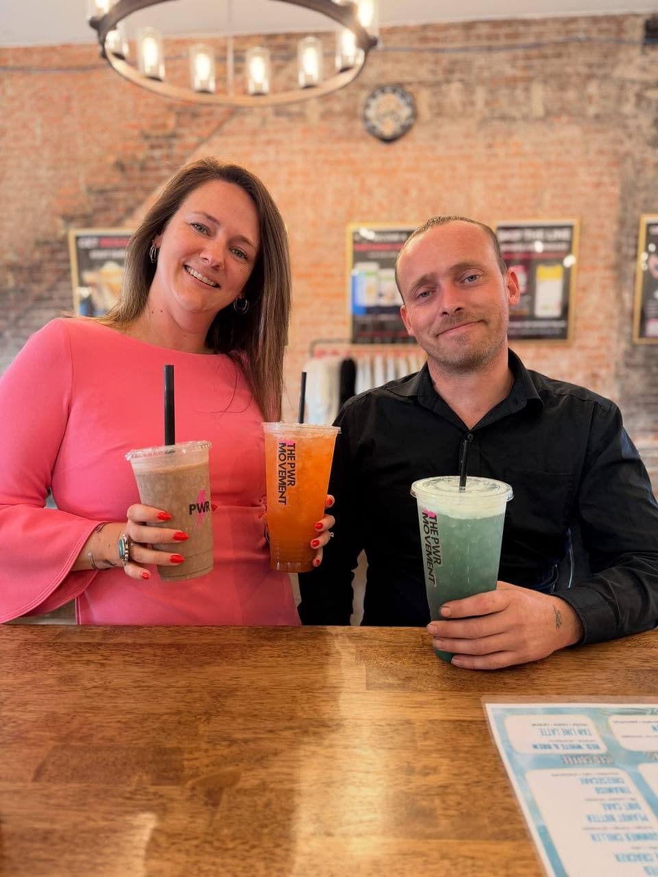 Founders Athena and Derek smiling behind the counter with a shake and two colorful mega teas